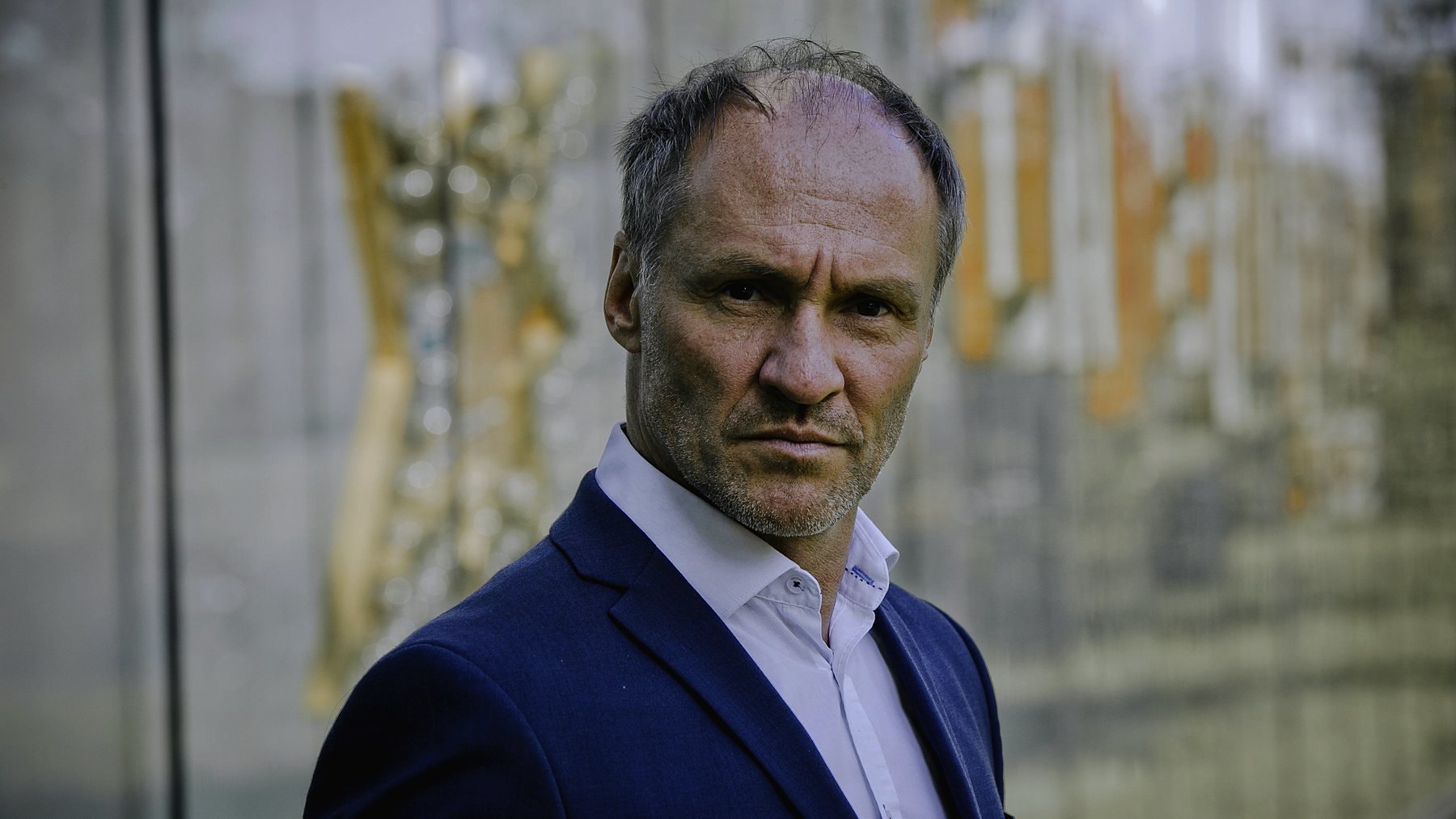 Armin Stockerer im blauen Anzug vor einer Glasfassade, Blick zur Seite — Foto: Christian Hartmann