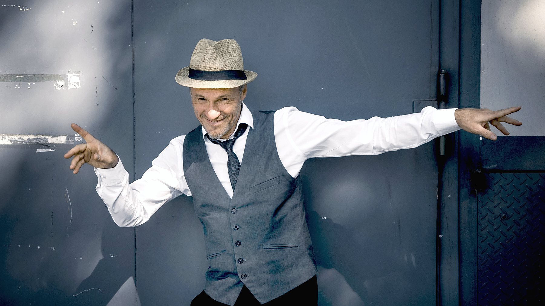 Armin Stockerer mit Hut und Weste, Arme ausgebreitet in einem dunklen Tor — Foto: Christian Hartmann